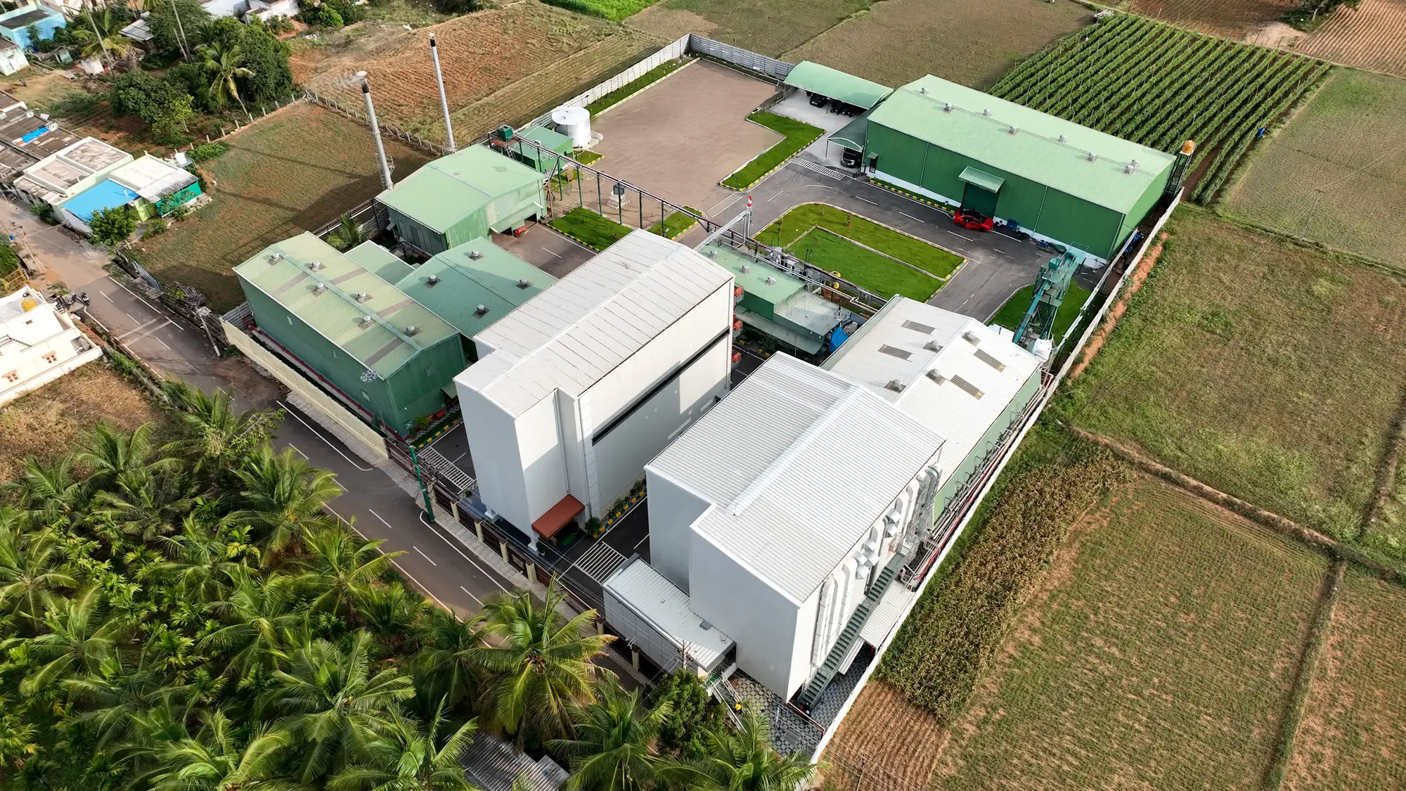 Aerial view of the Greenspace Herbs campus: white extraction and research blocks and green production sheds among coconut groves
