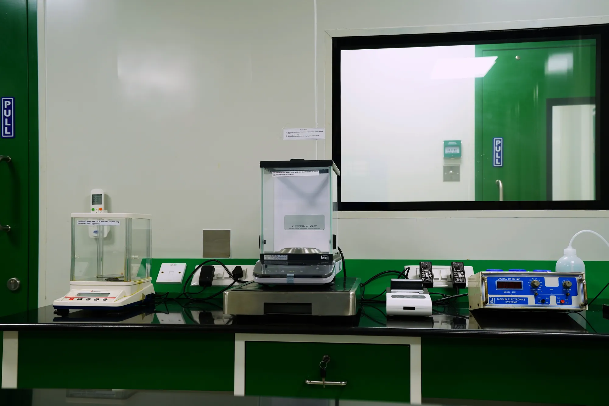 An analytical balance and bench instruments beneath an observation window