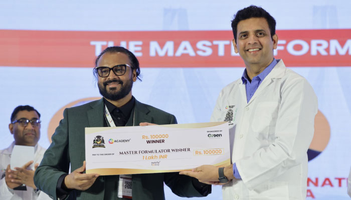 Two men on a stage pose with a large ceremonial cheque during an awards ceremony, with a banner in the background referencing the Master Formulator event.