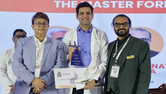 Three men on stage at an awards ceremony; the center man holds a blue glass trophy and a certificate.