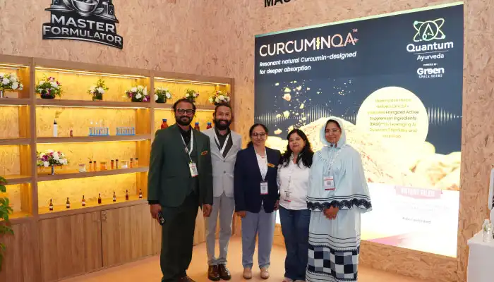 Five people stand together at a trade-show booth featuring CURCUMINA branding, with wooden shelves of jars on the left and a large product banner on the right.